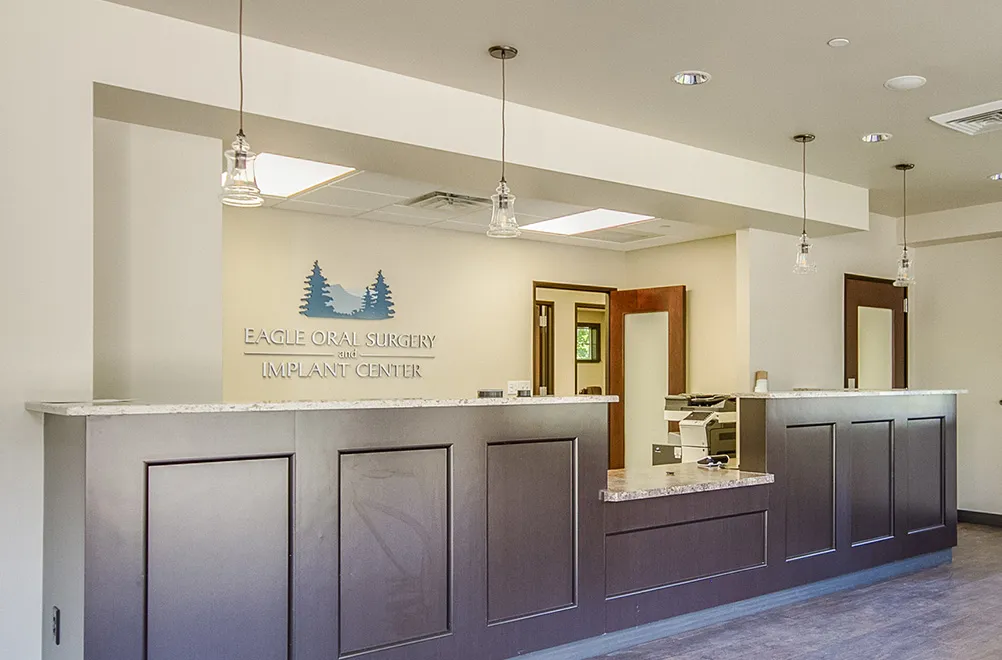 The front desk of Eagle Oral Surgery  Implant Center, made of rich dark wood and a granite countertop. The lighting is warm and inviting.